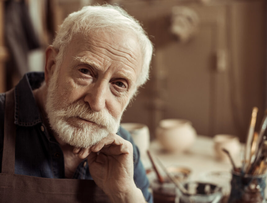 Portrait of senior potter in apron sitting at table and looking at camera Chrześcijanin w pracy